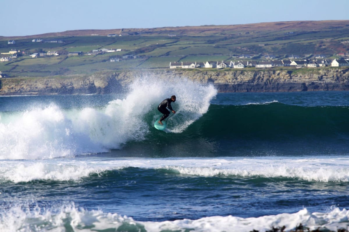 A surfer riding a wave with a coastal town in the background.