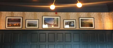 A room with a blue paneled wall, a chandelier with multiple bulbs, and five framed pictures.