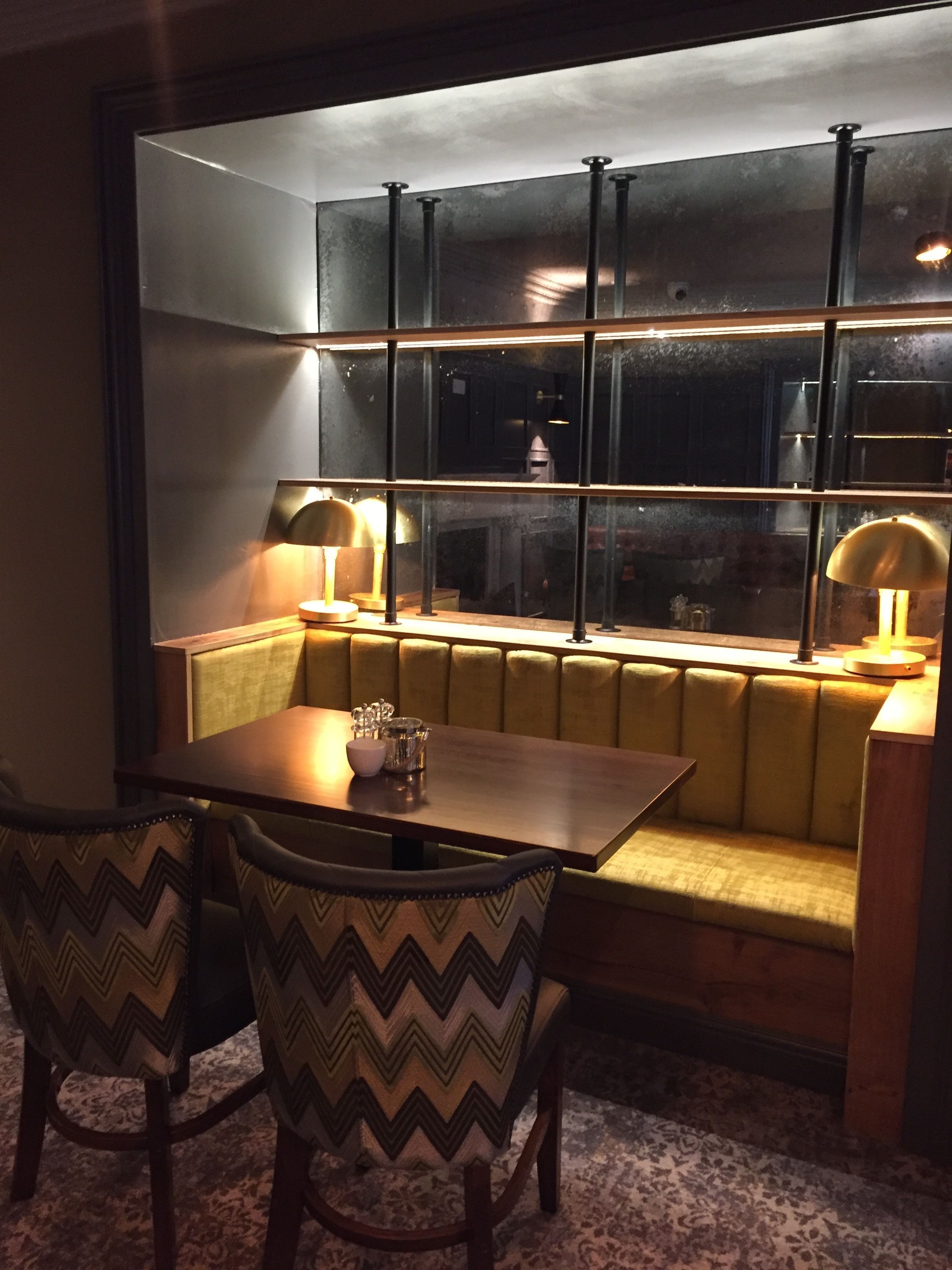 A cozy dining area with a wooden table and two upholstered chairs, a cushioned bench, and a large window with metal frames.