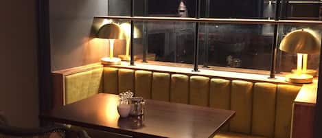 A cozy dining area with a wooden table and two upholstered chairs, a cushioned bench, and a large window with metal frames.