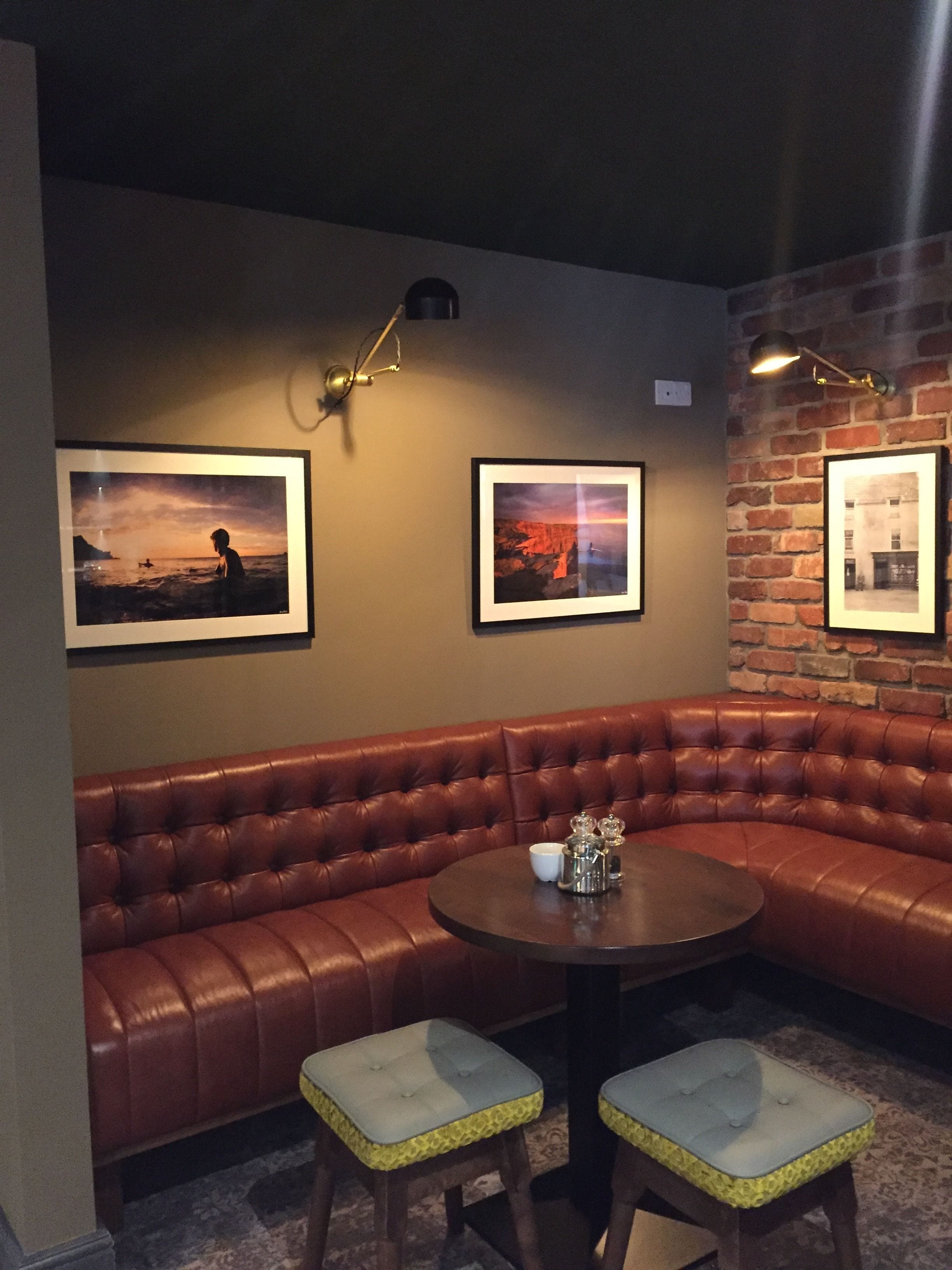 A cozy corner with a brown leather sofa, two matching stools, a small round table, and three framed pictures on the wall.