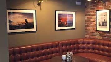 Un coin accueillant avec un canapé en cuir marron, deux tabourets assortis, une petite table ronde et trois tableaux encadrés accrochés au mur.
