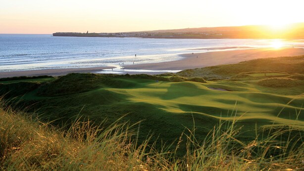 Een golfbaan aan de kust met uitzicht op de zee en een zonsondergang.