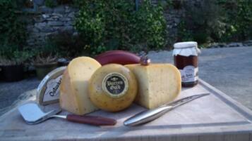 A wooden cutting board with a cheese wheel, a knife, a red object, and a jar of honey.
