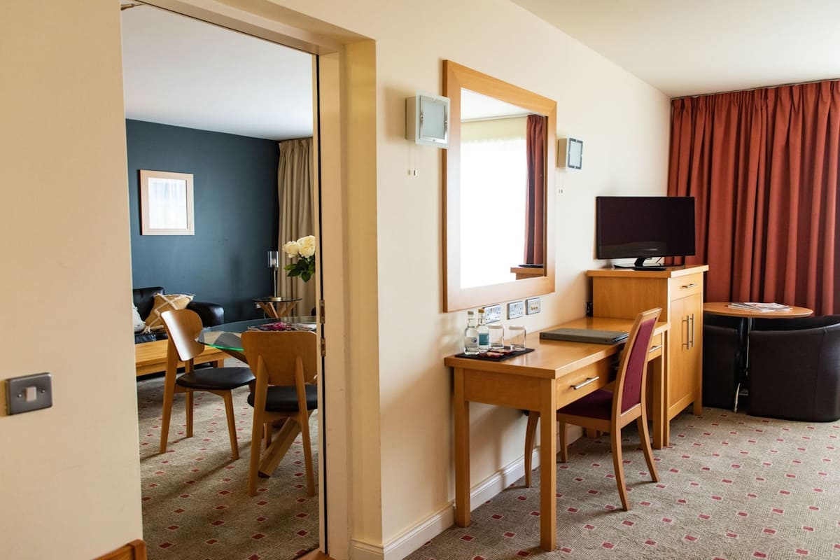 Ein Hotelzimmer mit Schreibtisch, Stühlen, einem Fernseher, einem Spiegel und einem Fenster mit Vorhängen.