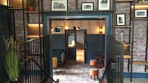 Een modern interieur met een trap die leidt naar een eetgedeelte, met een bakstenen muur, ingelijste foto's en een kamerkleed met een patroon.