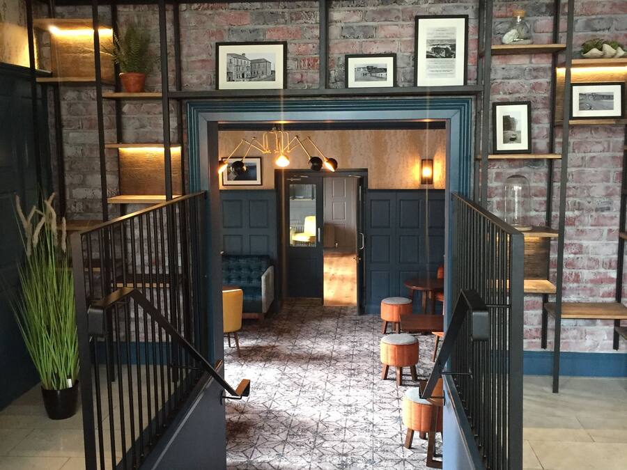 Un intérieur moderne avec un escalier menant à une salle à manger, agrémentée d’un mur en briques, de tableaux encadrés et d’un tapis à motifs.