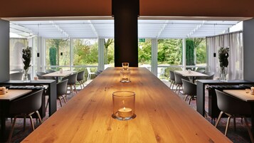 Una larga mesa de madera con velas en un comedor moderno con ventanas grandes y sillas.