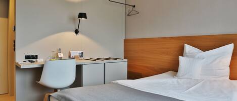 Una habitación de hotel con una cama, un escritorio, una silla y una lámpara fijada a la pared.