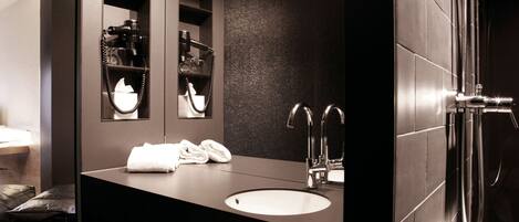 A modern bathroom with a dark countertop, a large mirror, a sink, and a shower area.