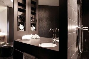 Un baño moderno con encimera oscura, un espejo grande, un lavabo y una zona de ducha.