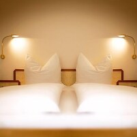 Una cama bien hecha con sábanas blancas y dos lámparas de noche a cada lado.