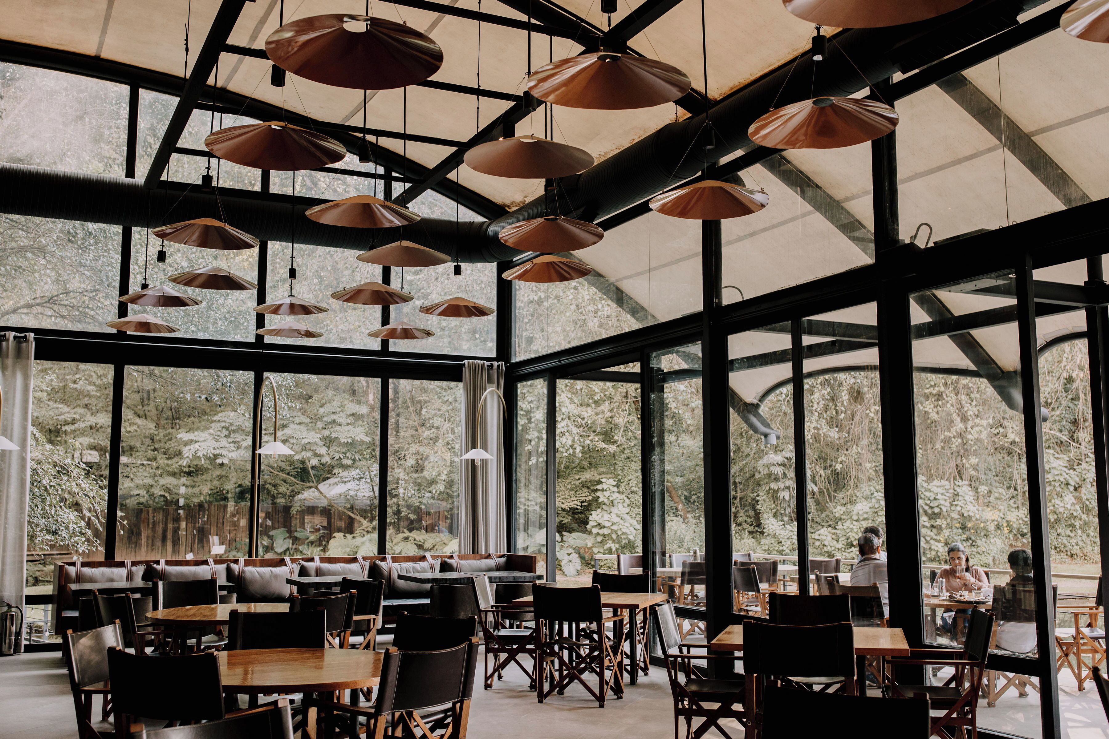 A spacious restaurant with large windows, wooden tables, and hanging pendant lights.