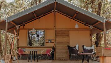 A rustic cabin with a wooden deck, two tables, and two chairs.