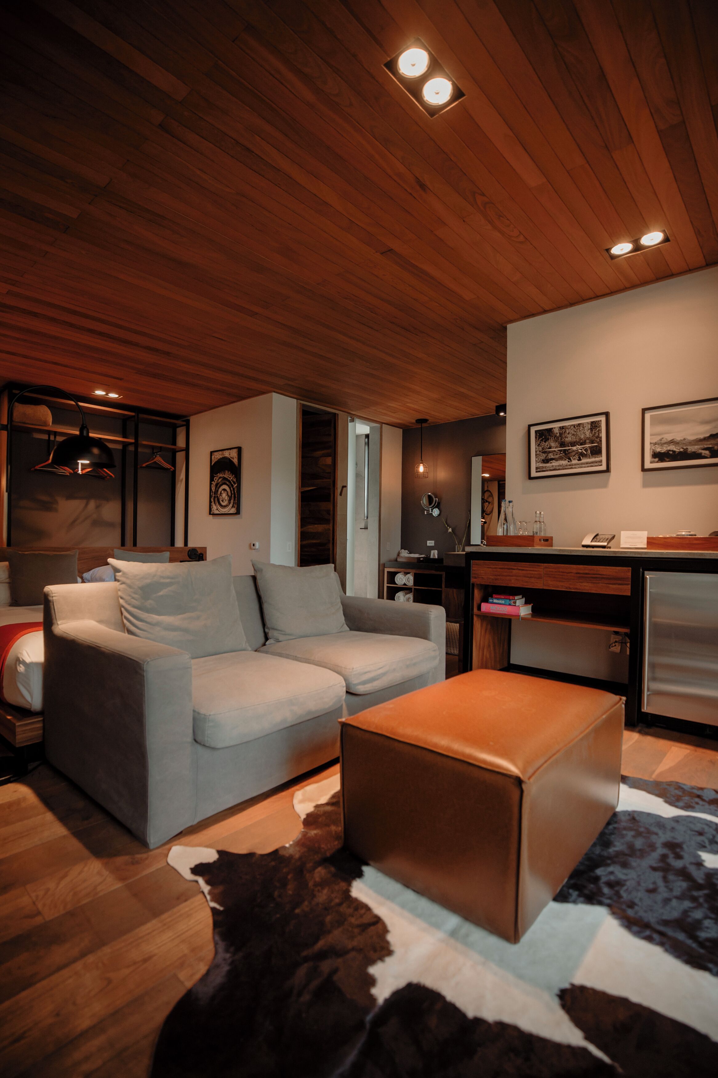 Una sala de estar moderna con un sofá, un reposapiés y techo de madera.