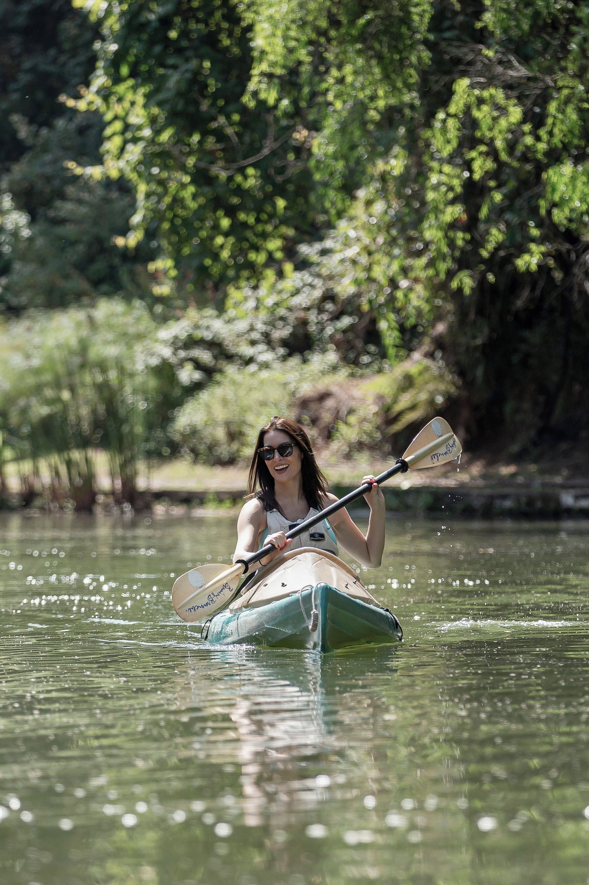 A person in a kayak on a calm body of water surrounded by greenery.