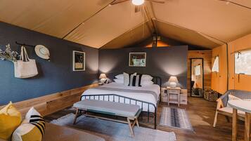 A tented room with a bed, bedside tables, a bench, and a chair.