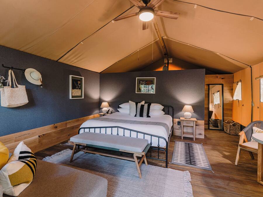 A tented room with a bed, bedside tables, a bench, and a chair.