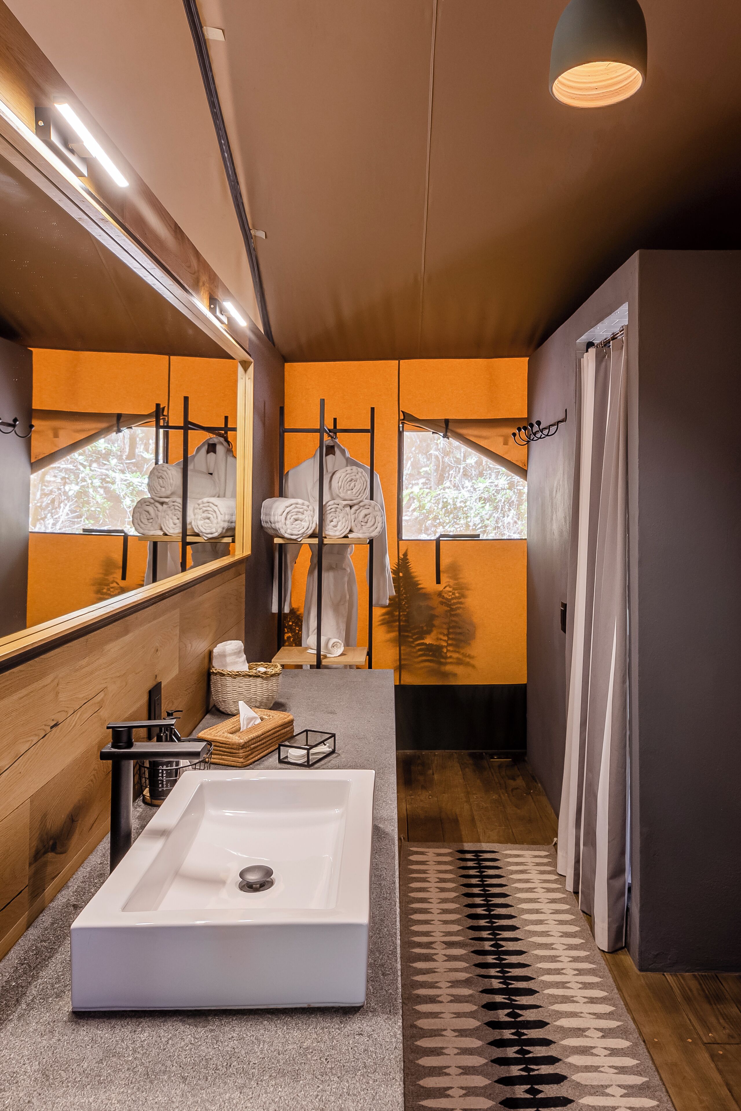 Un baño moderno con un lavamanos grande de color blanco, detalles de madera y un espejo que refleja vistas al exterior.