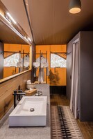 Un baño moderno con un lavamanos grande de color blanco, detalles de madera y un espejo que refleja vistas al exterior.