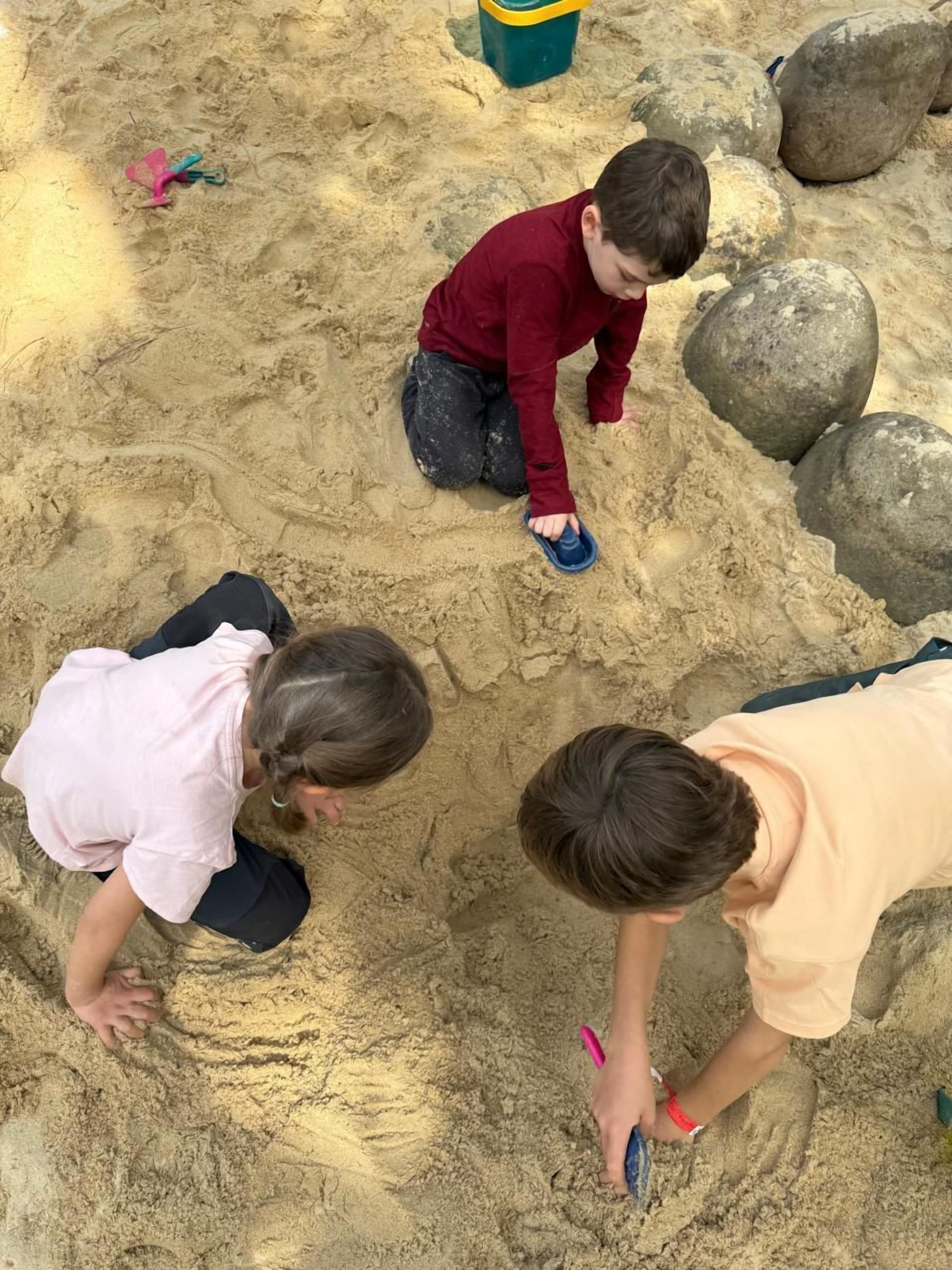 A sandy area with rocks and children playing.