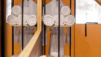 Un baño con un banco de madera, un perchero con toallas enrolladas, una cesta y una mesita con una vela y pañuelos.