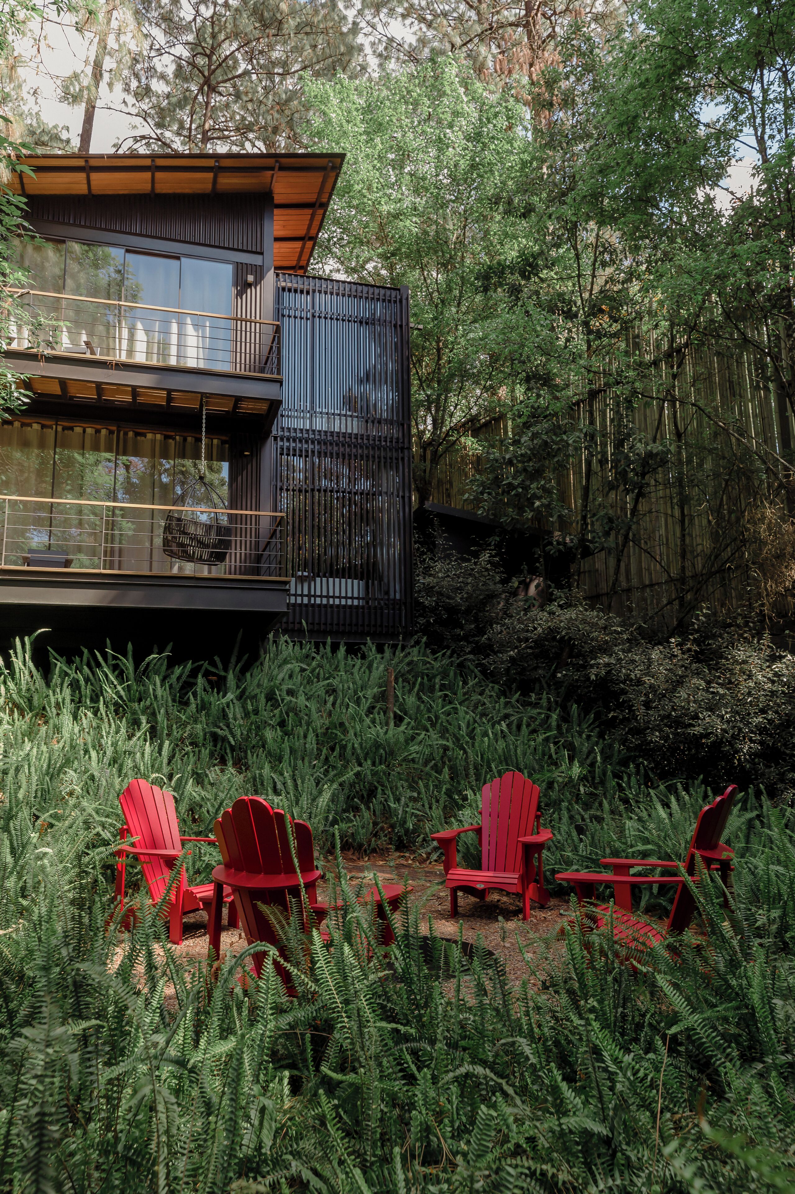 A modern house with a balcony and outdoor seating area surrounded by dense greenery.