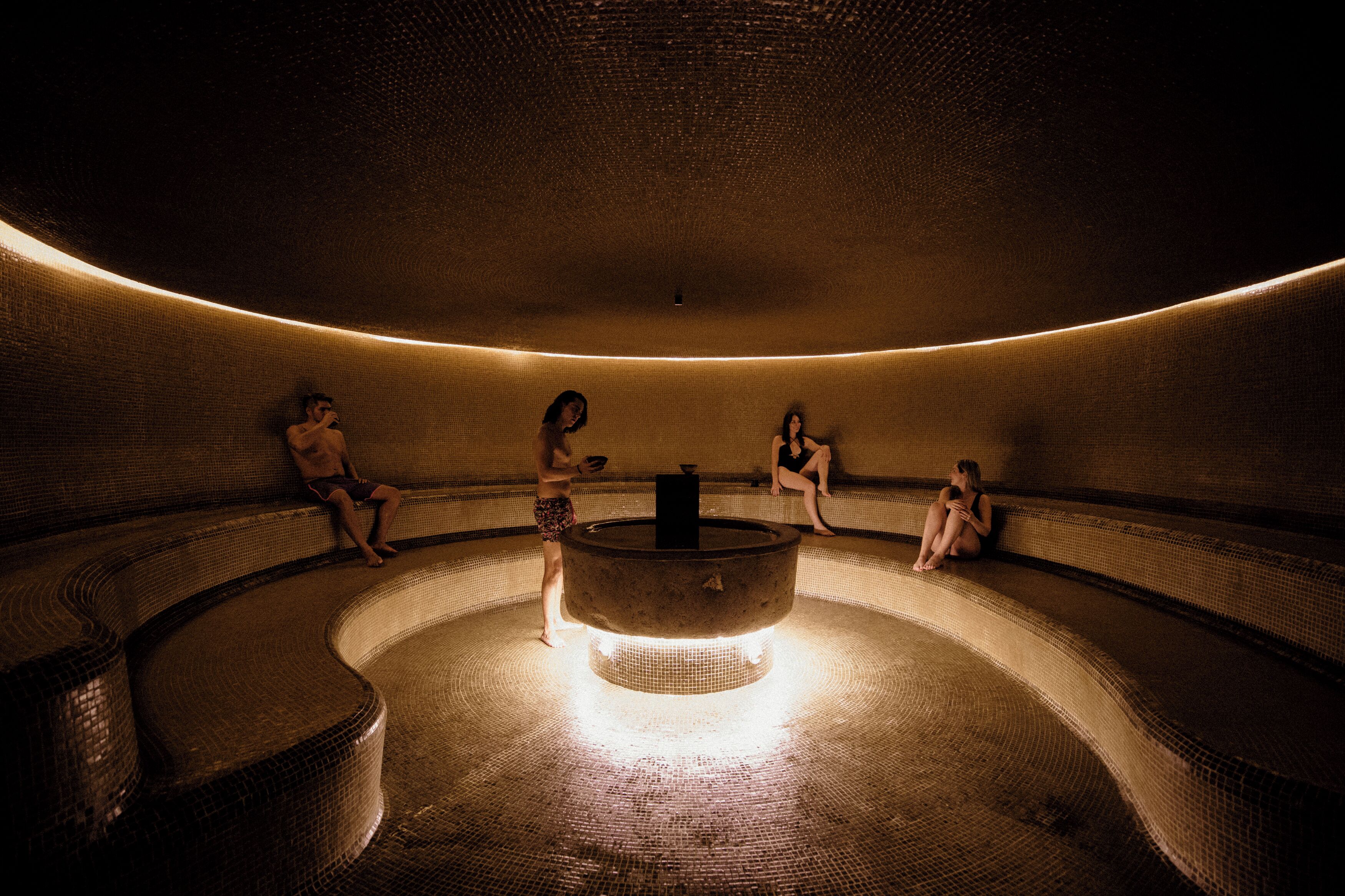 A circular, dimly lit room with a central water feature and tiled walls.
