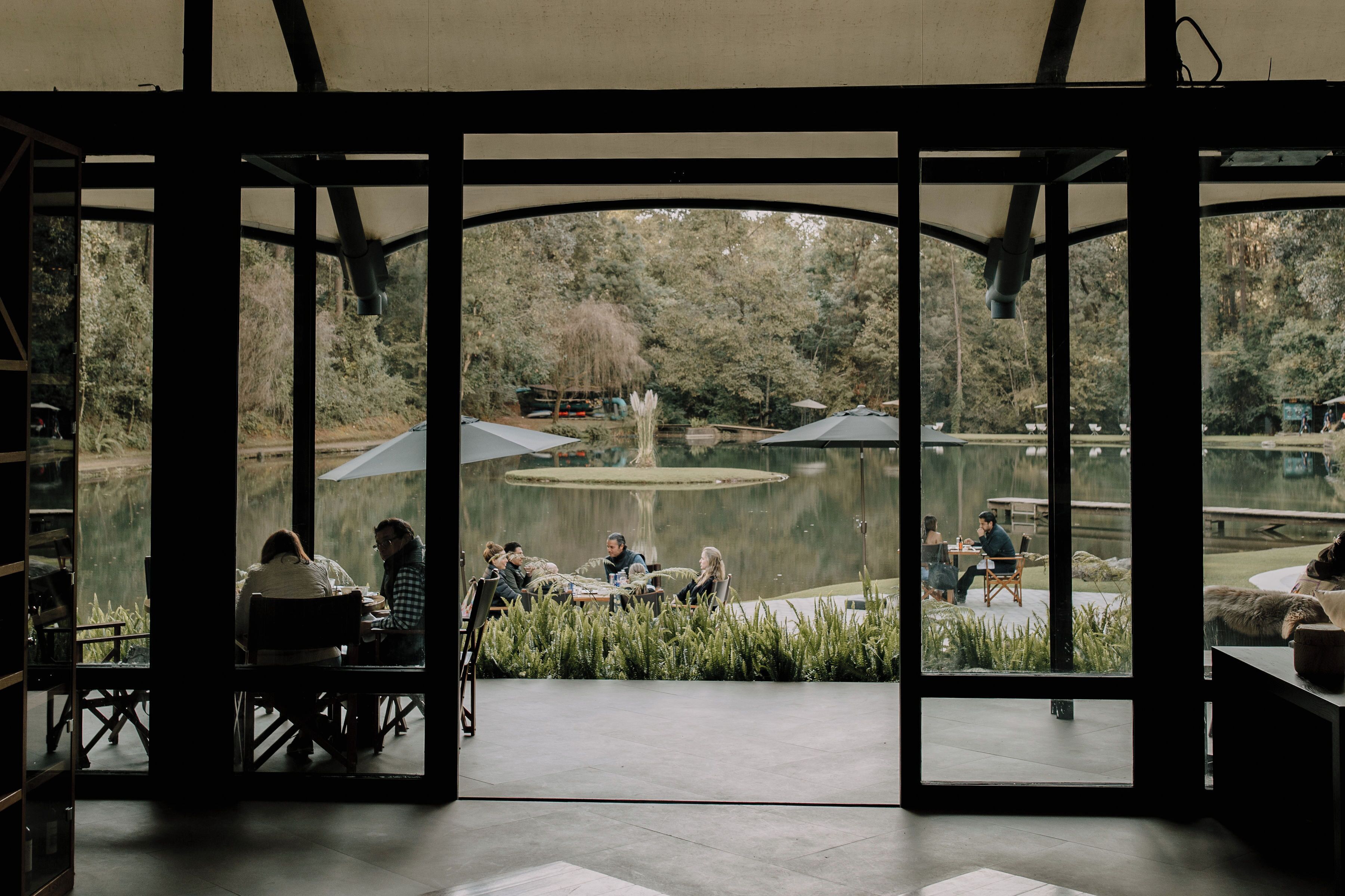 An indoor dining area with large windows overlooking a pond and trees.