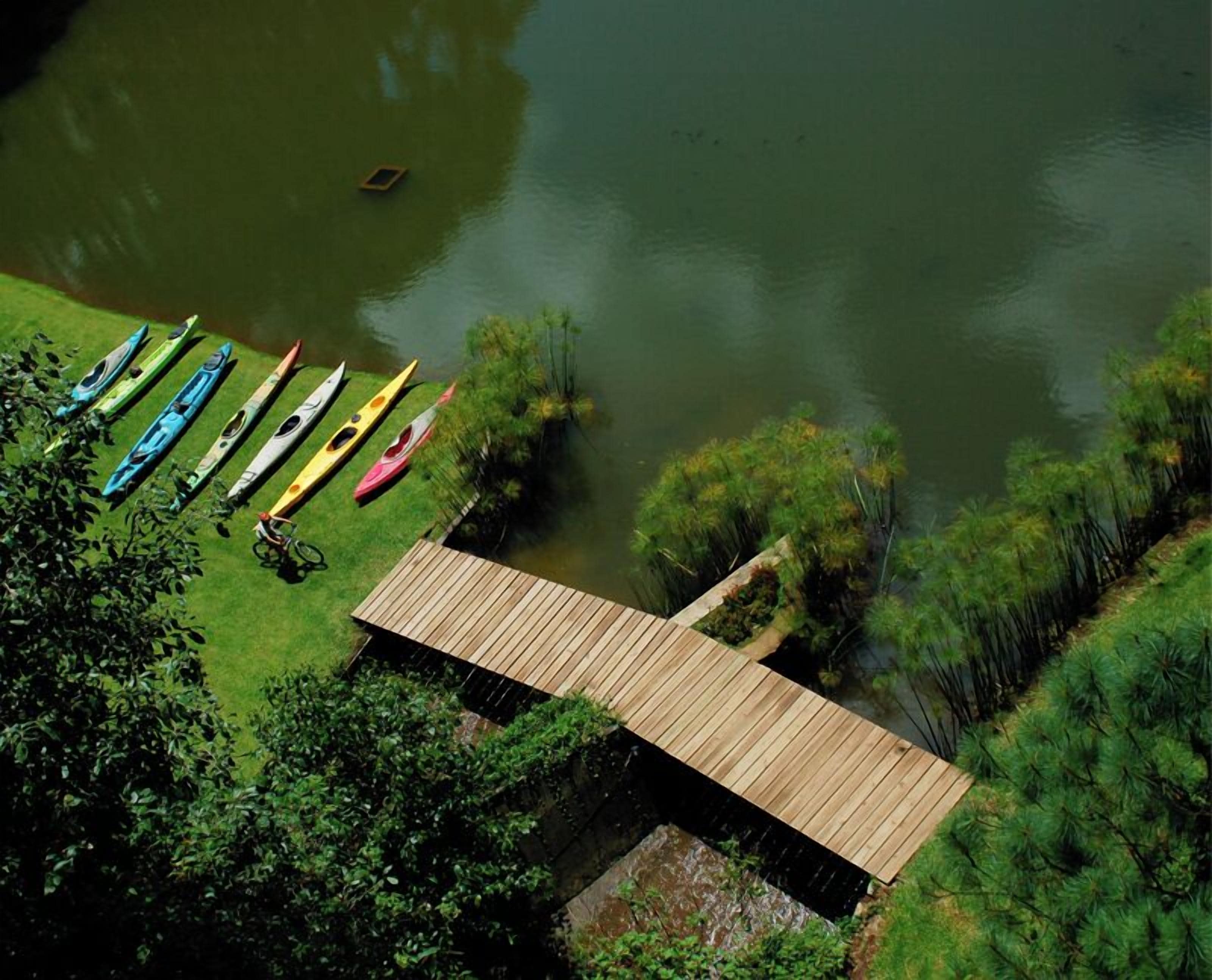 A wooden dock extending into a lake with kayaks lined up on the grassy shore.