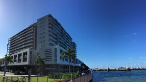 A modern multi-story hotel with balconies, a waterfront view, and a marina in the background. - Cairns Private Apartments (Cairns)