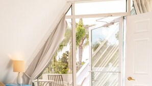 Een slaapkamer met een bed, nachtkastje, lamp en uitzicht op een balkon met een tafel en stoelen.