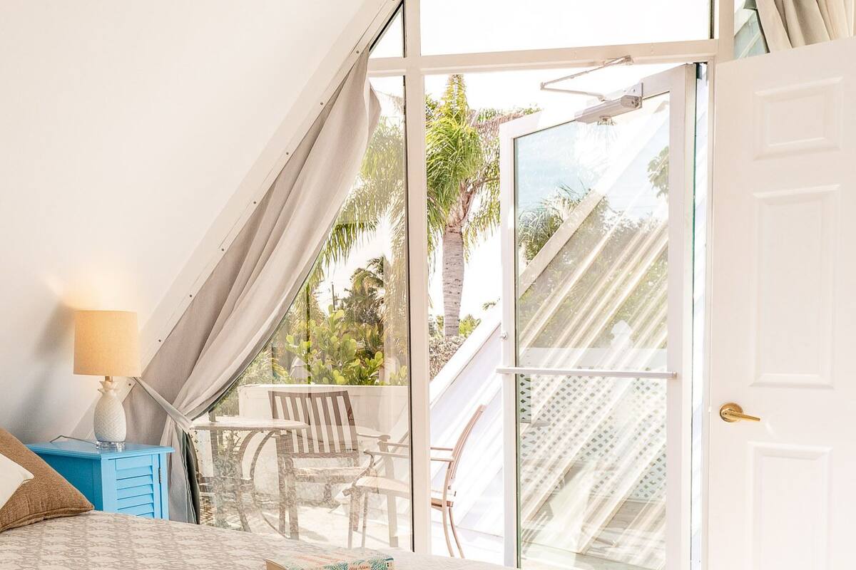 A bedroom with a bed, a nightstand, a lamp, and a view of an outdoor balcony with a table and chairs.