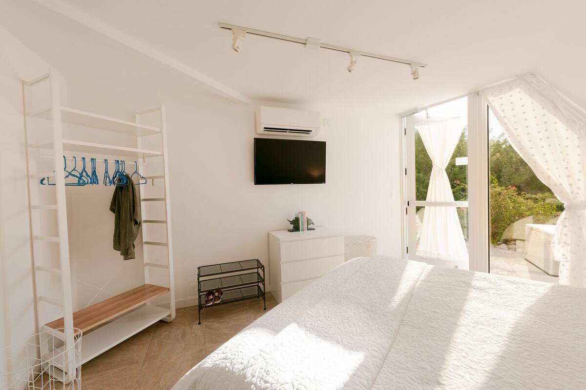 A bedroom with a bed, a wardrobe, a TV, and a window with curtains.
