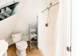 A bathroom with a toilet, a towel rack with towels, and a shower area.