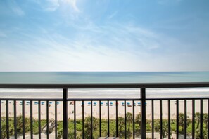 A beach view from a balcony with a railing, palm trees, and beach umbrellas.