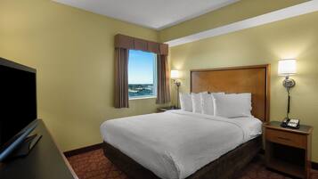 Habitación de hotel con una cama grande, un televisor, una mesita de noche con lámpara y una ventana con cortinas.