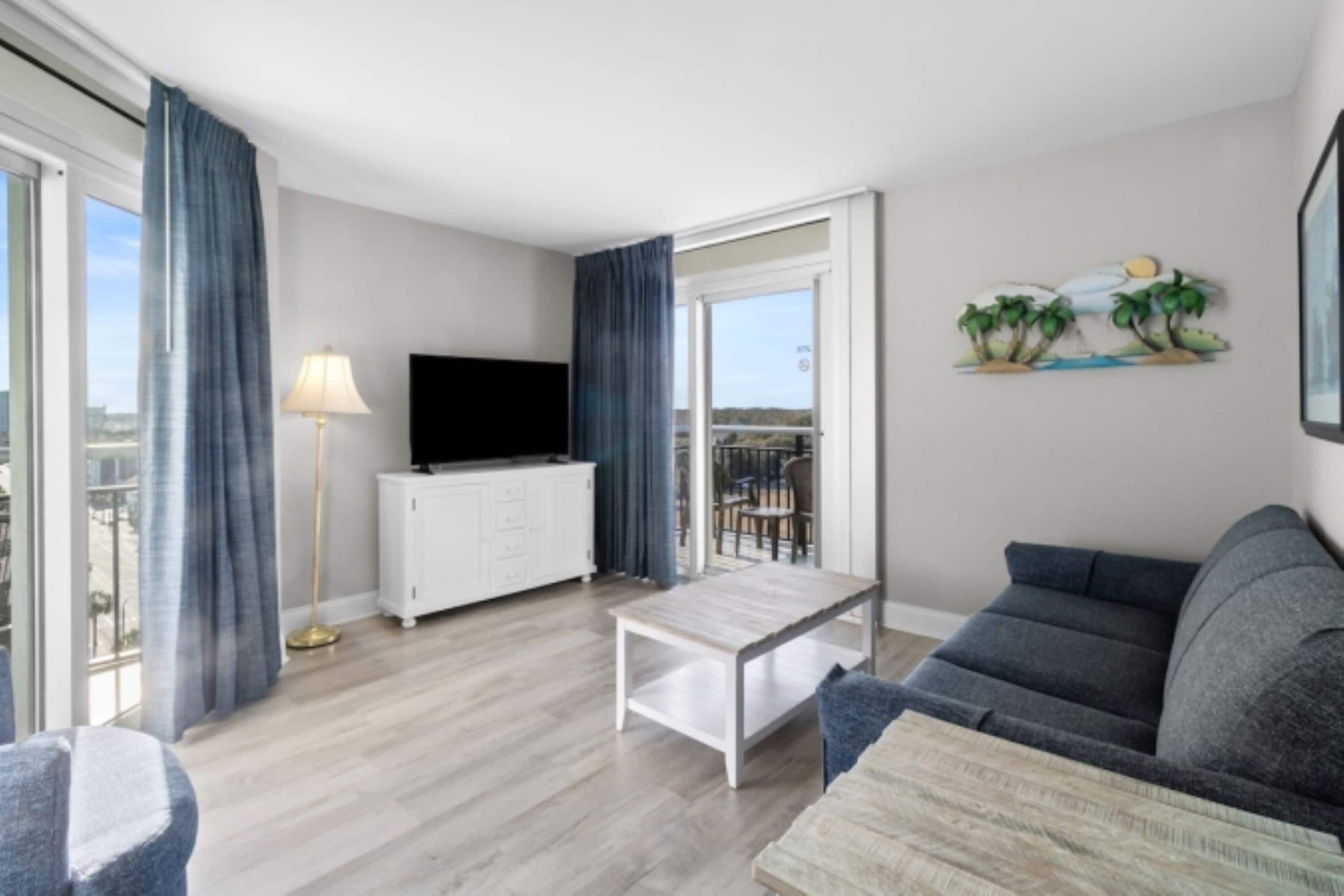 Una sala de estar moderna con una televisión de pantalla plana, un sofá, una mesa de centro y un balcón con vistas.