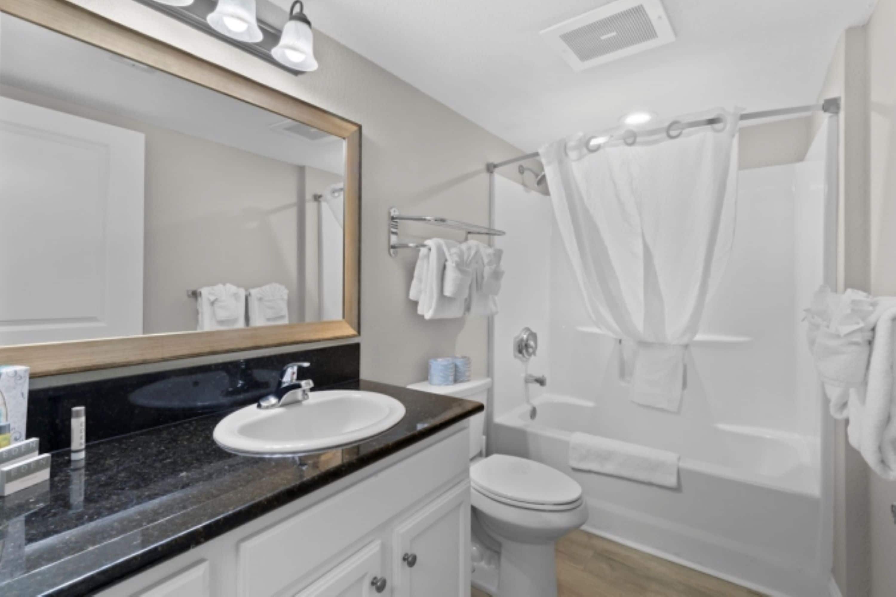 Un baño moderno con lavamanos, espejo y bañera blancos.
