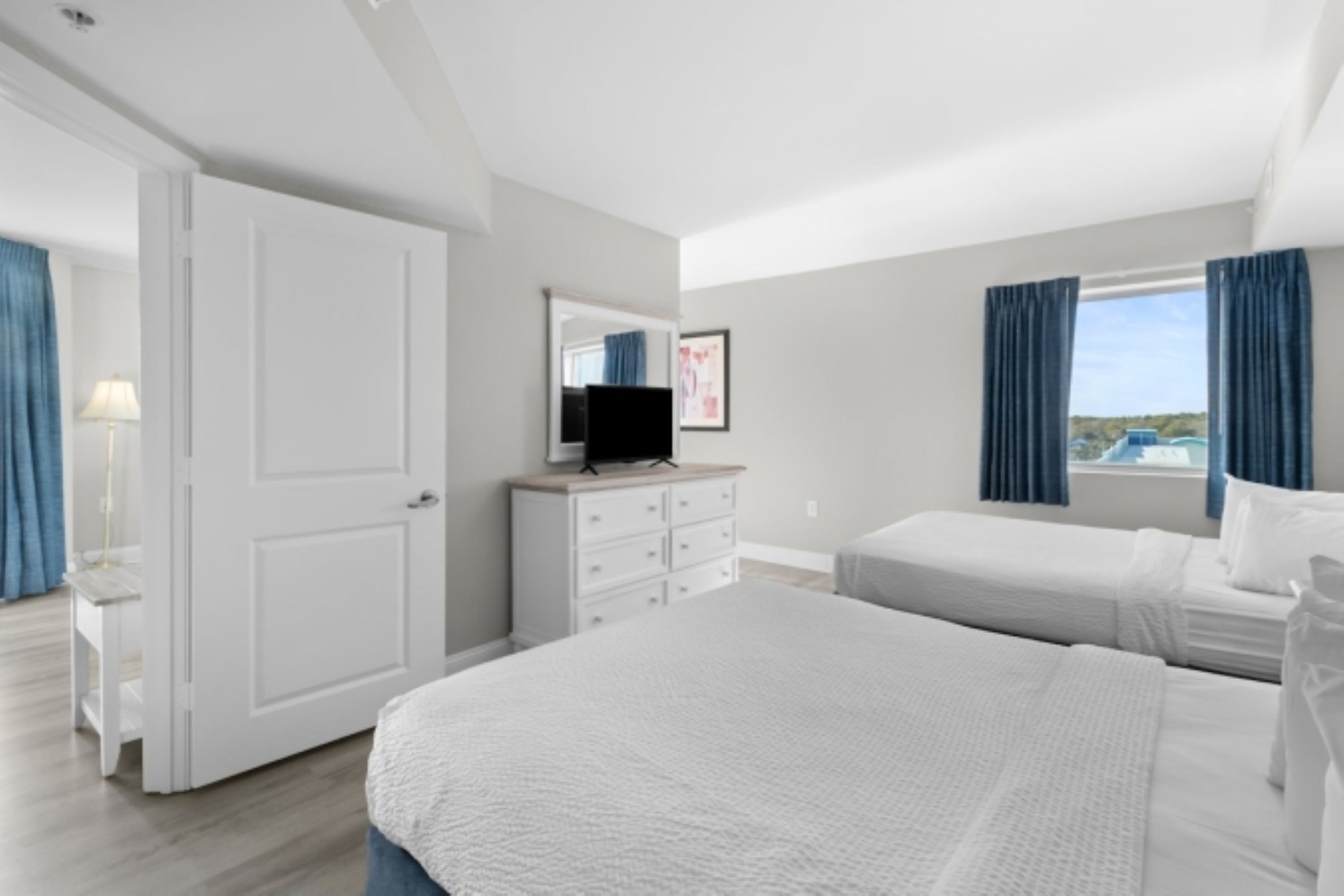 A bedroom with a large bed, a dresser, a TV, and a window with curtains.