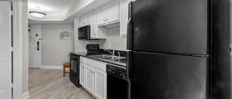 Una cocina moderna con armarios blancos, un refrigerador negro, un microondas y un lavavajillas.