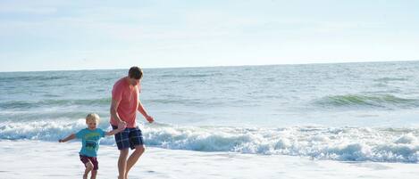 A beach scene with a man and a child walking along the shore.