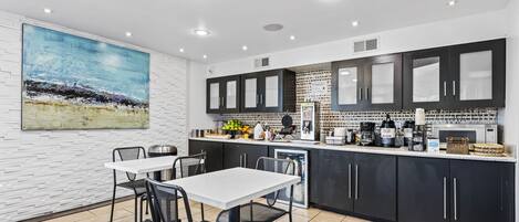 A modern kitchen with a white table and chairs, black cabinets, and a large painting on the wall.