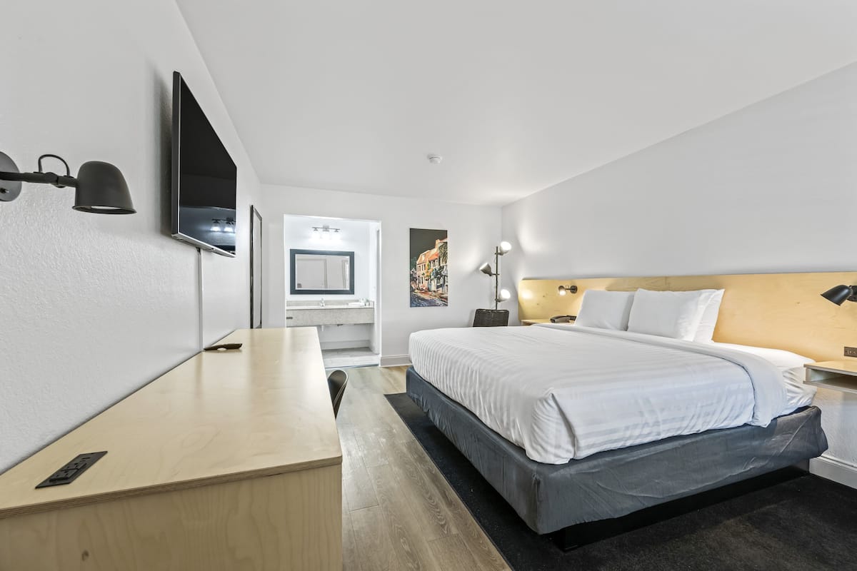 A modern hotel room with a large bed, a desk, a flat-screen TV, and a bathroom visible through an open door.