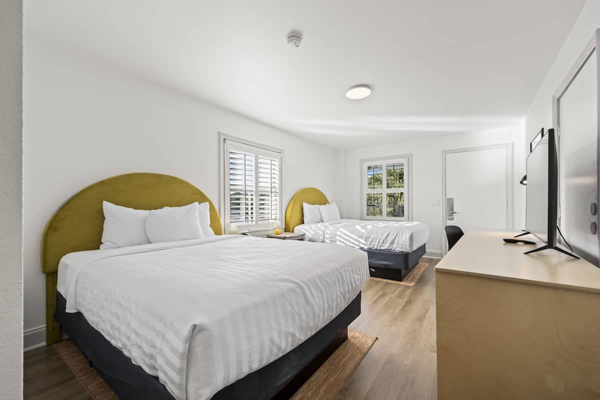 A modern hotel room with two beds, a desk, and a TV.