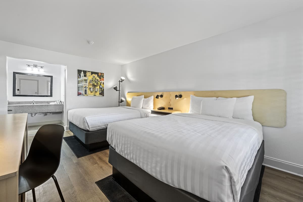 A hotel room with two beds, a desk, a chair, a mirror, and a nightstand with a lamp.