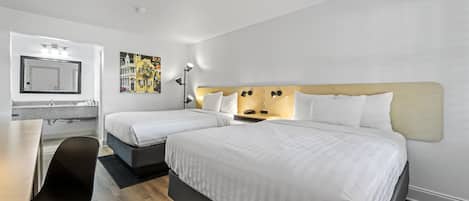 A hotel room with two beds, a desk, a chair, a mirror, and a nightstand with a lamp.