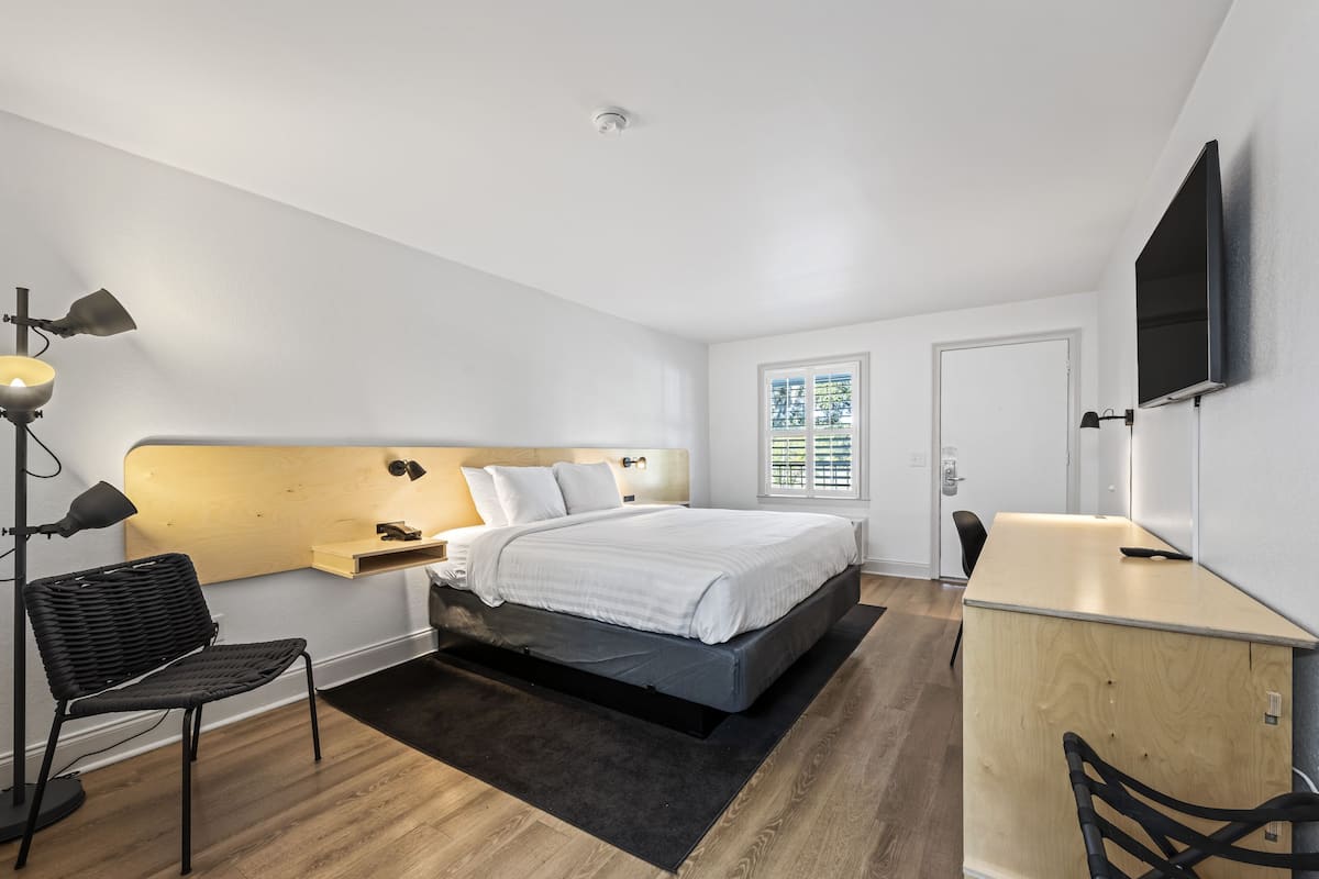A modern bedroom with a bed, bedside table, lamp, and a desk with a chair.
