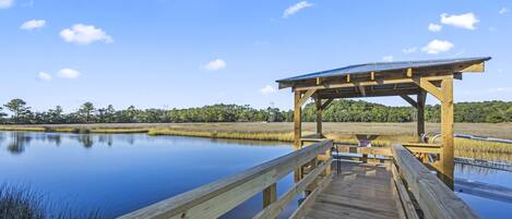A wooden pier leading to a covered area with a solar panel roof, surrounded by calm water and greenery.
