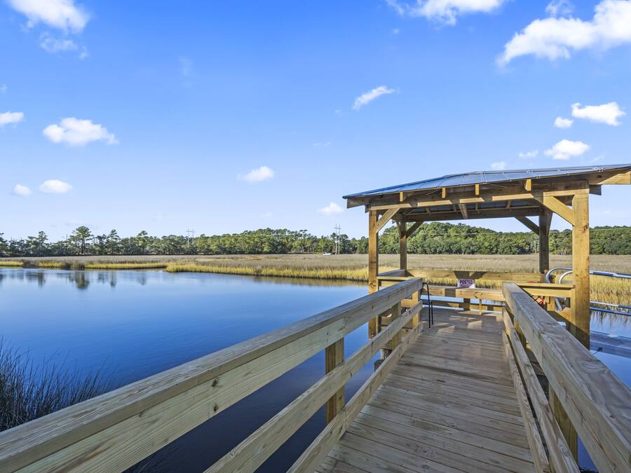 A wooden pier leading to a covered area with a solar panel roof, surrounded by calm water and greenery.